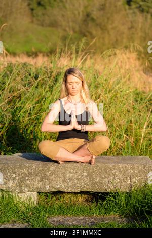 Frau in Lotussitz mit Namaste-Händen, die draußen Yoga und Achtsamkeit praktiziert Stockfoto