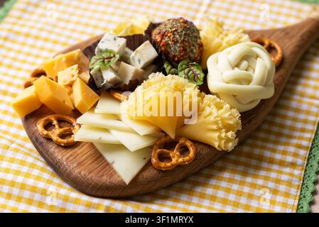 Nahaufnahme eines gemischten Käsebretts auf einer hölzernen Servierplatte mit Cheddar-Würfeln, geschnittenem Käse, Blauschimmelkäse-Stücken, mit Kräutern überzogener Käsekugel, Brezel Stockfoto