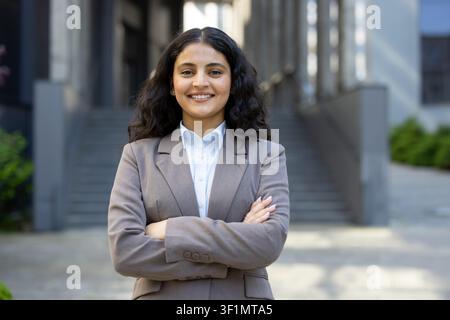 Ermächtigender junger Profi steht selbstbewusst mit verschränkten Armen vor einem Bürogebäude und repräsentiert Karriererfolg, Führung und eine glänzende Zukunft im Geschäftsleben Stockfoto