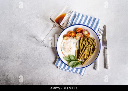 Minimalistisches Brunch-Teller mit fermentiertem Spargel, Spiegelei, Kirschtomate und Basilikum auf weißem Teller mit blauem Rand, gestylt auf gestreifter Serviette mit Stockfoto