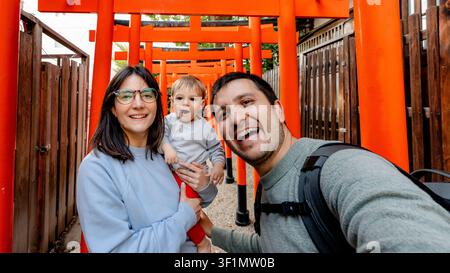 Eine fröhliche Familie macht ein Selfie an den farbenfrohen Torii-Toren des Horikoshi-Schreins in Osaka, Japan. Die leuchtend orangefarbenen Tore bilden eine beeindruckende Kulisse Stockfoto