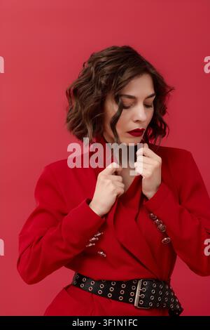 Stylische junge brünette Frau posiert anmutig in einem schicken roten Outfit vor einem hellen Hintergrund Stockfoto