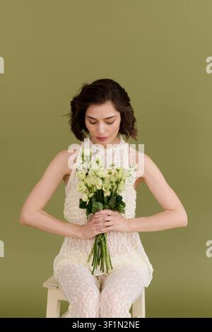 Brünette Model posiert anmutig mit Blumen, während sie in einem schicken Spitzenensemble gekleidet ist Stockfoto