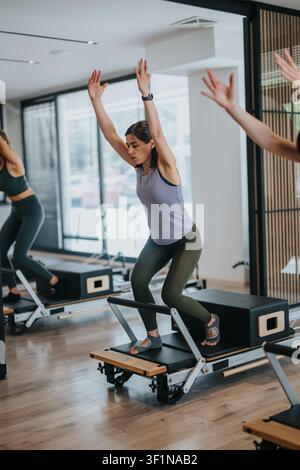 Frau macht Reformer-Pilates-Training in einem modernen Studio mit erhobenen Armen während der Übungseinheit Stockfoto