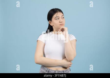 Nachdenkliche junge Frau, die den Finger am Kinn hält und im Studio weg schaut Stockfoto