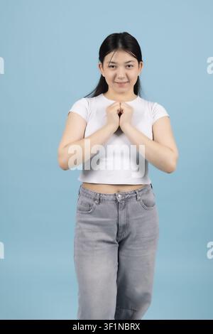Ruhige junge Frau hält die Hände in Gebetshaltung und lächelt im Studio Stockfoto
