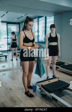 Zwei Frauen bereiten sich auf ein Pilates-Reformer-Training in einem hellen Fitnessstudio vor Stockfoto
