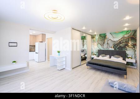 Helles Studioapartment mit modernem Interieurdesign, das einen Küchenbereich, einen Schlafbereich mit einer grünen Marmorakzentwand und schlanke weiße Möbel umfasst Stockfoto