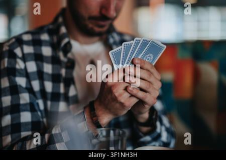Mann hält Spielkarten und konzentriert sich auf ein Poker-ähnliches Kartenspiel in einer lockeren Umgebung Stockfoto