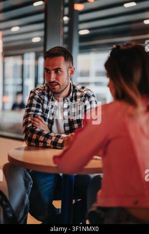 Junger Mann in einem karierten Hemd unterhält sich mit einem Begleiter an einem Cafétisch während eines lockeren Gesprächs Stockfoto