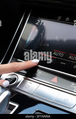 Weibliche Hand berührt die Klimaanlage-Option auf dem digitalen Armaturenbrett in einem Luxusfahrzeug. Nahaufnahme, die sich auf die Aktivierung der Klimaanlage des Autos konzentriert und Stockfoto