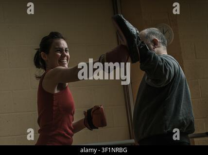 Glückliche Frau, die mit ihrem Trainer in einem dunklen Fitnessstudio Schattenboxen trainiert Stockfoto