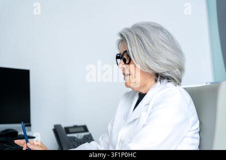 Ärztin im höheren Alter, die einen Laborkittel und eine Brille trägt und medizinische Informationen erklärt Stockfoto