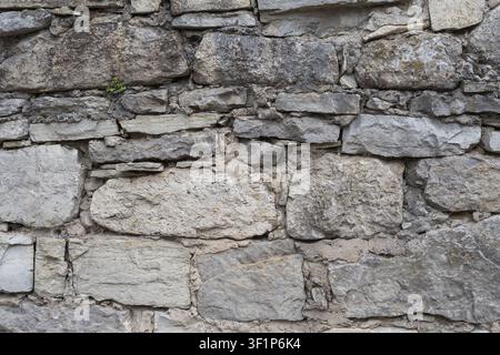 Verwitterte Steinmauer aus unregelmäßigen Natursteinen und Mörtel. Rustikale Mauerstruktur für Architektur, Restaurierung und Design. Stockfoto