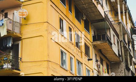 Alte gelbe Wohnhausfassade mit Balkonen und Wäsche zum Trocknen. Stockfoto