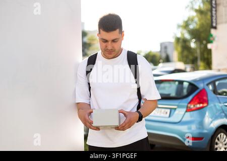 Ein lächelnder Typ hält ein Paket draußen an einem sonnigen Tag Stockfoto