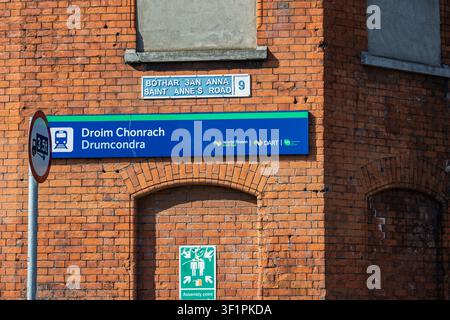 Nahaufnahme des Schildes des Bahnhofs Drumcondra und eines klassischen blauen Dubliner Straßenschildes an einer rotbacksteinernen Fassade. Stockfoto