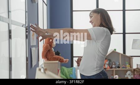 Frau zeigt mit dem Finger auf die Zeichnung des Kindes an der Wand im Kindergartengebäude und fördert so das Wachstum der frühen Bildung. Stockfoto
