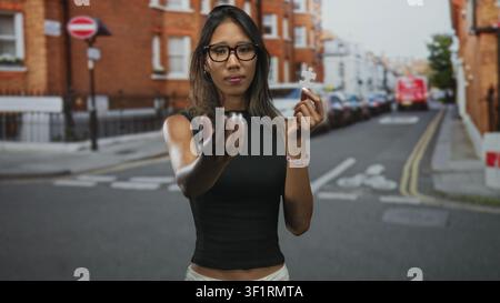 Thailändische Frau mit Brille hält ein weißes Puzzleteil in der rechten Hand und streckt die linke Hand in Richtung Kamera auf einer Straße; Verbindung neugierig. Stockfoto
