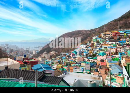 Farbenfrohe Hügel-Dächer des Gamcheon-Kulturdorfs in Busan, Südkorea, mit blühenden Kirschbäumen am Berghang und sichtbarern Hafen Stockfoto