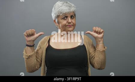 Frau zeigt in einem grauen Studio die Daumen auf die Brust, trägt Tanktop und Strickjacke mit Basketball und Armbändern; Selbstvertrauen. Stockfoto