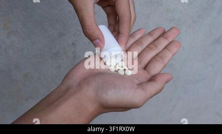 Hand schüttet weiße Medizinpillen aus einer Flasche Stockfoto