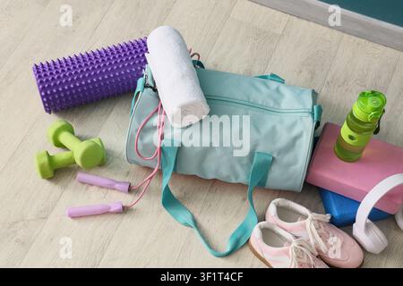 Fitness-Turnbeutel mit Trainingsgeräten wie Hanteln, Schaumstoffrolle und Springseil auf einem Holzboden Stockfoto