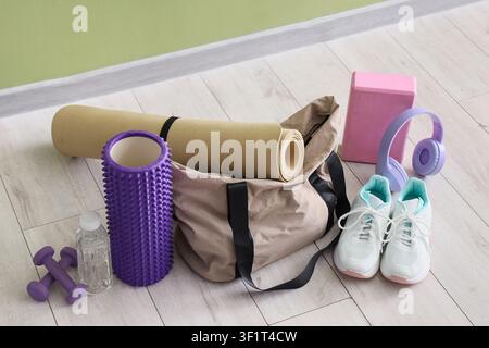 Fitnessgeräte und Zubehör einschließlich einer Yogamatte, einer Schaumstoffrolle, Hanteln und Turnschuhen auf einem hellen Holzboden Stockfoto