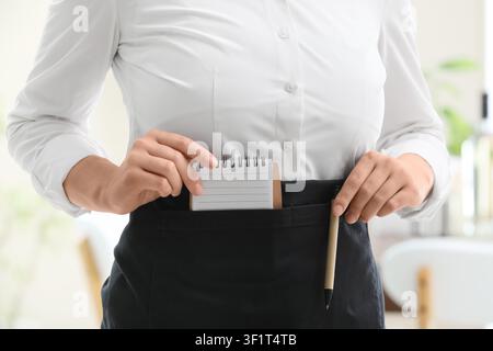Kellnerin oder Kellner zieht einen kleinen Notizblock und einen Stift aus der Schürzentasche, bereit, eine Bestellung aufzunehmen Stockfoto