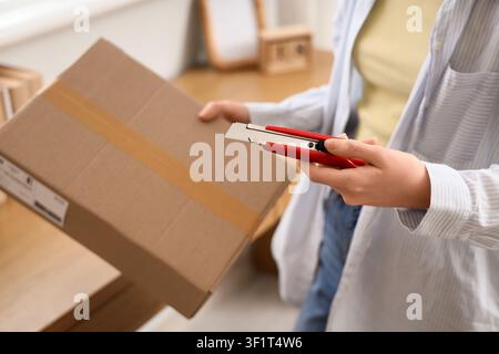 Frau hält ein rotes Universalmesser, um einen Karton zu öffnen, Paketzustellung und Auspacken Stockfoto