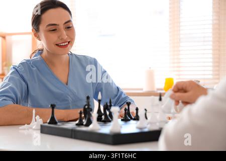 Physiotherapeutin mit einer älteren Frau, die Schach am Tisch in der Küche spielt Stockfoto