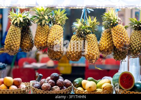 Hängende Ananas und gemischte tropische Früchte an einem lebhaften Marktstand in Phu Quoc in heller Umgebung Stockfoto