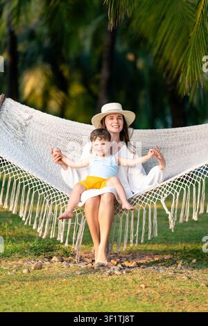 Mutter und Kind entspannen zusammen in einer weißen Hängematte in einem sonnigen Palmengarten in Phu Quoc Stockfoto