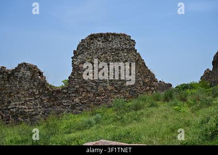 Alte verwitterte Stein-Festungsmauer mit grünem Gras unter blauem Himmel Stockfoto