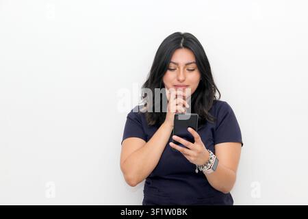 Fröhliche junge lateinamerikanische Frau zeigt auf ihr Smartphone in der Hand, Online-Shopping-Anwendung auf weißem Hintergrund Stockfoto