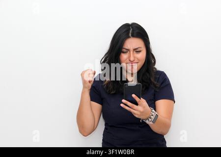 Fröhliche junge lateinamerikanische Frau zeigt auf ihr Smartphone in der Hand, Online-Shopping-Anwendung auf weißem Hintergrund Stockfoto