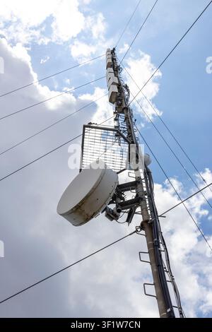 Telekommunikationsmast vor bewölktem Himmel, ausgestattet mit Antennen und einer Parabolantenne für moderne Kommunikation Stockfoto