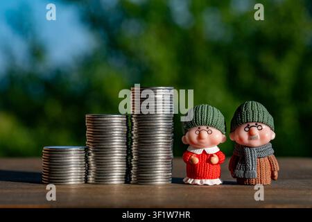 Miniatur-Seniorenpaar steht neben wachsenden Münzstapeln auf grünem Hintergrund, Nahaufnahme. Finanzkonzept der Rentenplanung, Seniorenpension Stockfoto
