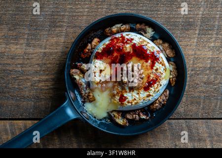 Ansicht von gebackenem Camembertkäse auf der Bratpfanne, Walnüsse, Honig und Marmelade auf Holztablett-Hintergrund, Nahaufnahme, Oberansicht Stockfoto