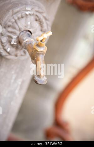 alter undichter Wasserhahn in einer heruntergekommenen Inneneinrichtung, möglicherweise ein Badezimmer oder eine Küche, Nahaufnahme, die sich auf das Waschbecken und die metallkeramischen Komponenten konzentriert, grau und Stockfoto