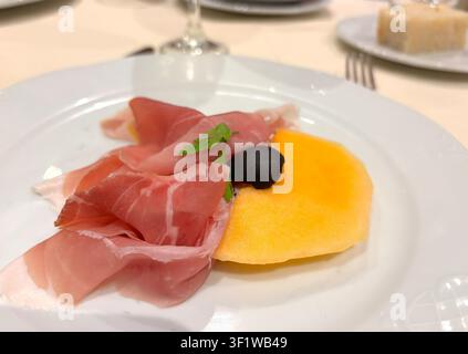 Scheiben Prosciutto auf weißem Teller. Spanischer Jamon geschnitten mit Melone im Restaurant, Makrofoto von Parmaschinken, Serrano oder Iberico auf unscharfem Hintergrund Stockfoto