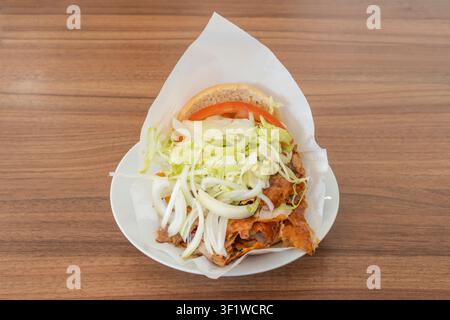 Doner-Kapsandwich mit gebratenem Fleisch, zerrissenem Salat und Pommes frites auf einem weißen Pappteller über einem rustikalen Holztisch. Stockfoto
