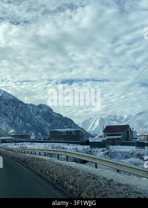 Schneebedecktes Bergdorf unter wolkigem Himmel, mit Häusern und schneebedeckten Gipfeln, Winterhintergrund. Mobilfoto Stockfoto