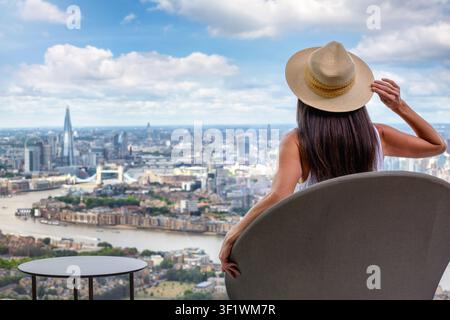 Rückansicht einer Frau, die auf einem Stuhl sitzt und die panoramische Sommeraussicht auf die Skyline von London, England, genießt Stockfoto