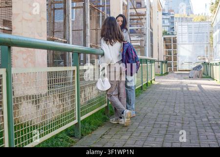 Zwei junge Frauen stehen an einem Zaun in einem Tiergehege. Sie teilen einen Moment des Lachens, während sie ihren Tag im Park besprechen. Die Sonne scheint oben. Stockfoto