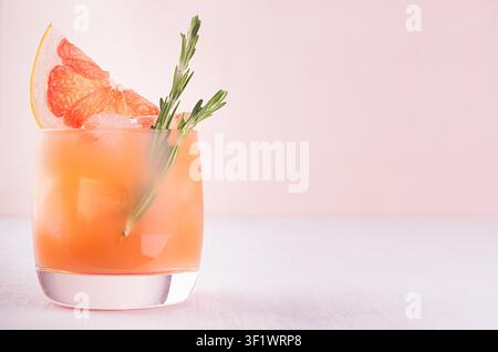 Kalter Sommercocktail mit Eiswürfeln, Saft und Grapefruitscheiben auf pastellrosa Hintergrund. Stockfoto