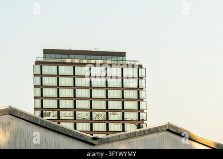 Modernes Glasbürogebäude, das sich hinter industriellen Dächern erhebt Stockfoto