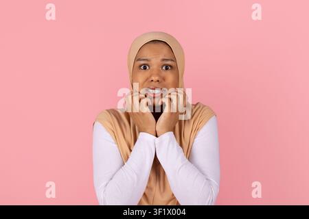 Ängstliche junge schwarze muslimische Frau in beigem Hijab, die sich im Stress das Gesicht berührt Stockfoto