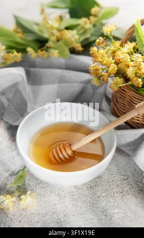 Lindenhonig in einer weißen Schüssel mit einem hölzernen Löffel, umgeben von Lindenblüten Stockfoto