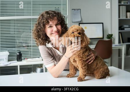 Porträt einer erwachsenen Frau, die einen Pudel in einer Tierarztpraxis hält Stockfoto